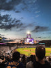 Baseball stadium crowd watching a game at dusk beneath floodlights and a scoreboard