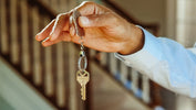 Hand holding a single house key on a metal keyring in a hallway