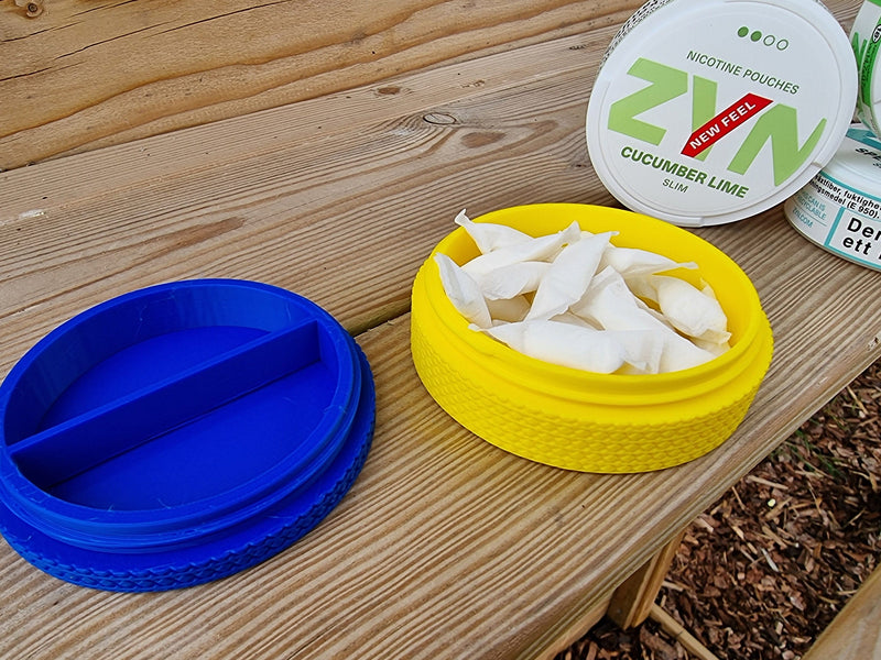 Open yellow pouch holder filled with nicotine pouches beside blue divider puck and ZYN tin