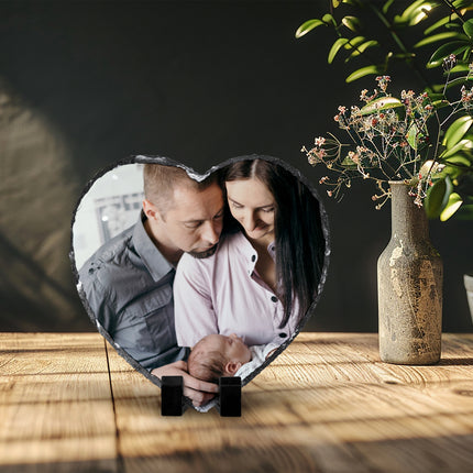 Freestanding heart-shaped photo slate displaying a new-parent photograph on a wooden shelf