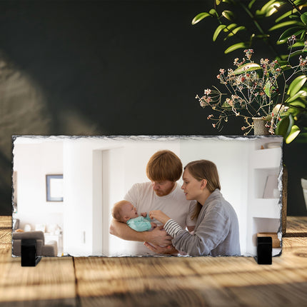 Freestanding rectangular photo slate displaying a new-parent photograph on a wooden shelf